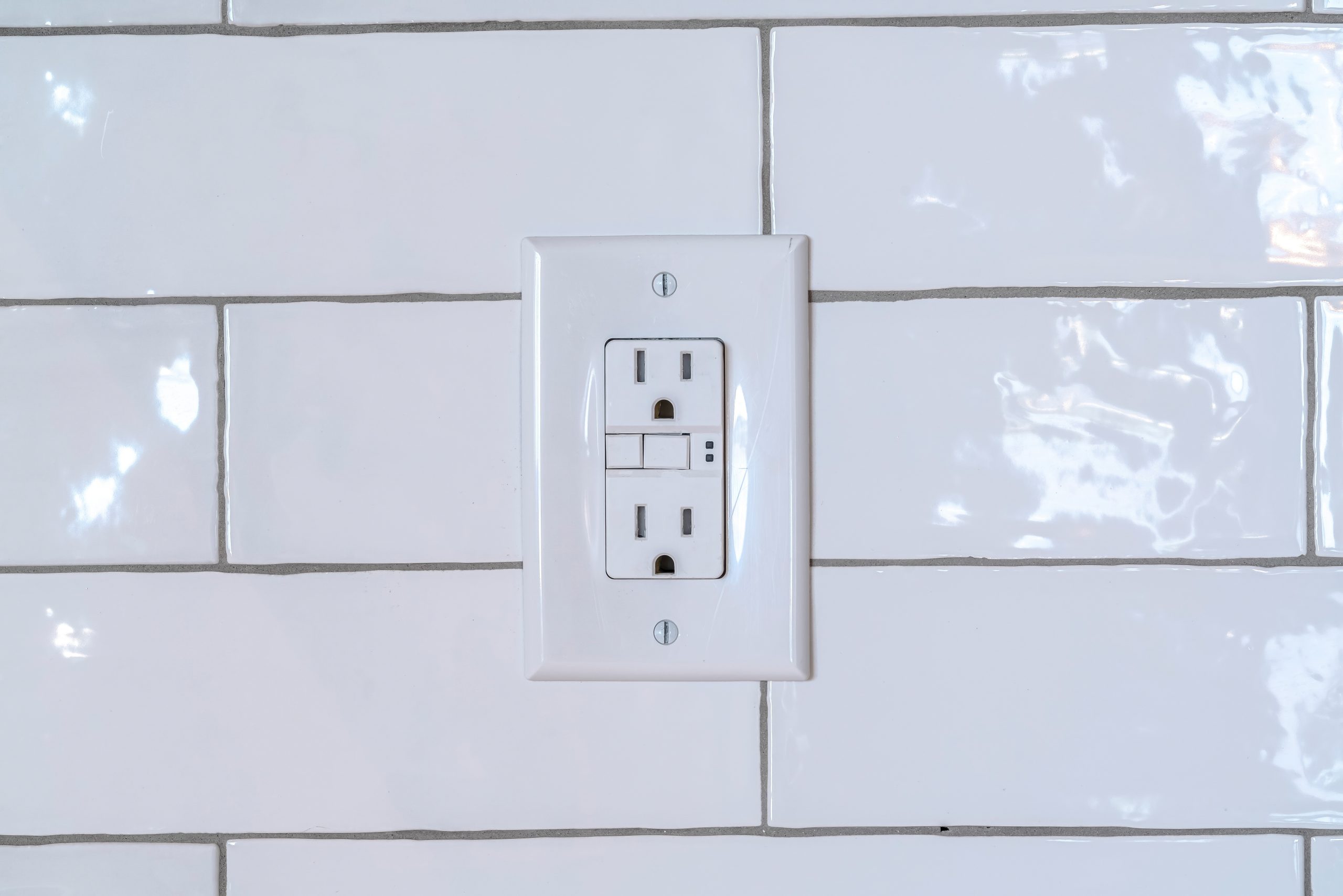 Three slot grounded receptacle for appliances against white tile wall of home. Close up of the electricity outlet fixture inside a house.